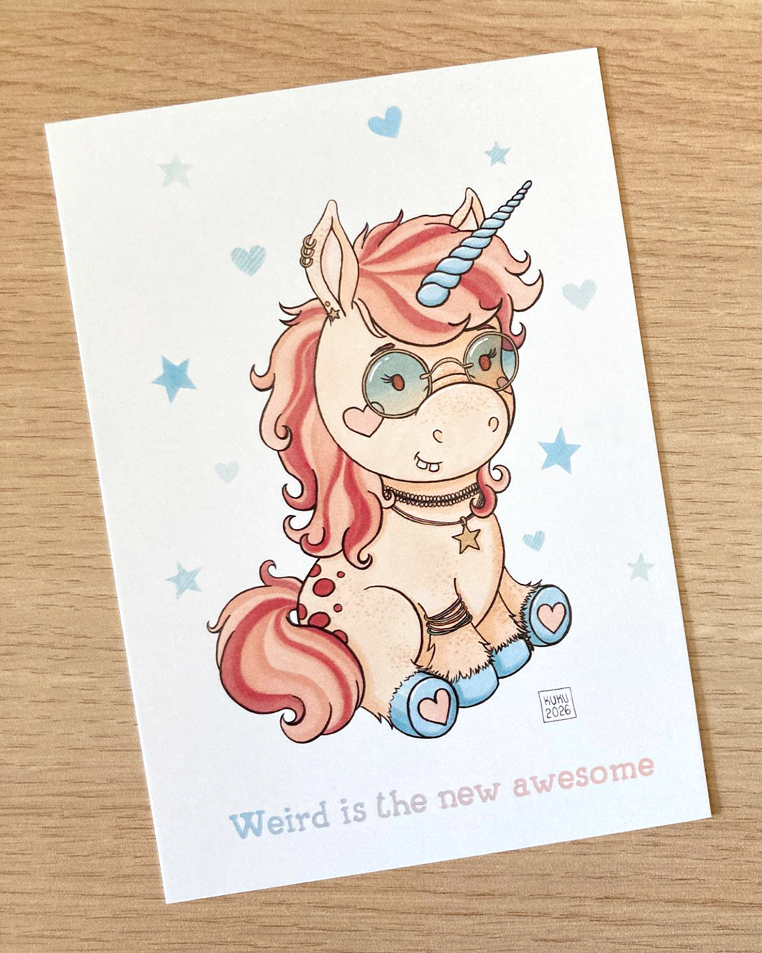 illustration d'une licorne portant des lunettes teintées et des piercing et bijoux avec la phrase "weird is the new awesome"